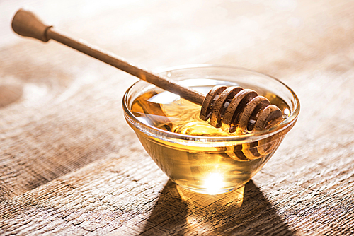 jar with honey and honey dipper on wooden table in sunshine