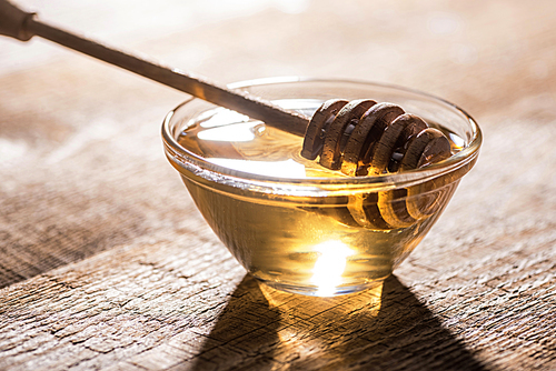 jar with honey and honey dipper on wooden table in sunlight