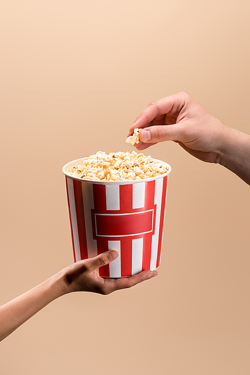 cropped shot of male and female hands with disposable bucket with popcorn isolated on beige
