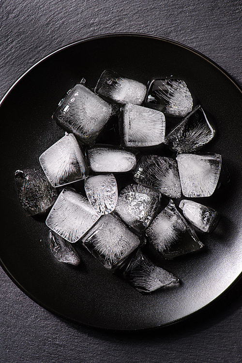 Ice cubes melting in black plate on dark background