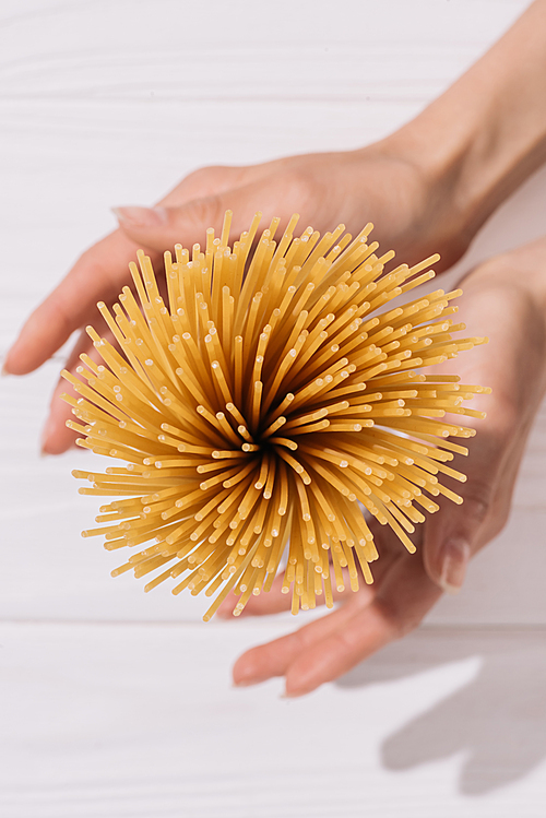 cropped shot of woman holding bunch of uncooked spaghetti over white wooden tabletop