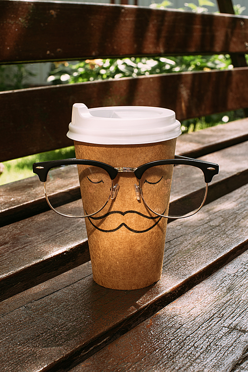 close up view of disposable cup with mustache sign and eyeglasses on wooden bench
