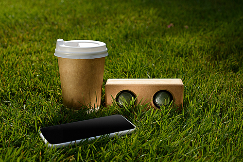 close up view of coffee to go, smartphone and audio speaker on green grass