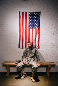soldier in military uniform with letter sitting on wooden bench with american flag on white brick wall behind, 4th july holiday concept