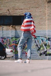 back view of woman with american flag in hands standing on street, 4th july holiday concept