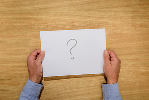 cropped image of man holding paper with question mark over wooden table