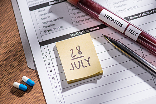 selective focus of stick it 28th july date, medical questionary, pills and test flask with lettering hepatitis test on table