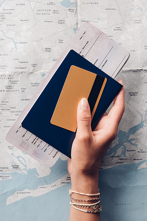 cropped shot of woman holding passport, ticket and credit card in hand with map on background, vacation concept