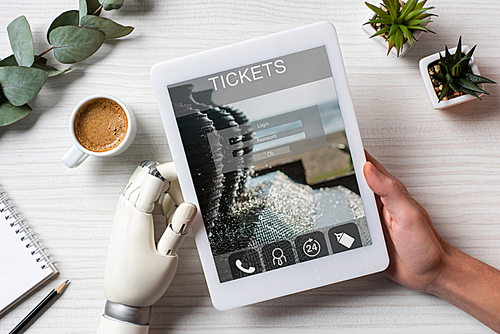 partial view of man with prosthesis arm using digital tablet with tickets on screen at table with coffee cup in office