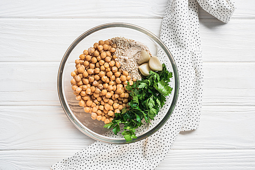 Top view of chickpeas, parsley and spices ingredients for hummus in bowl on wooden surface