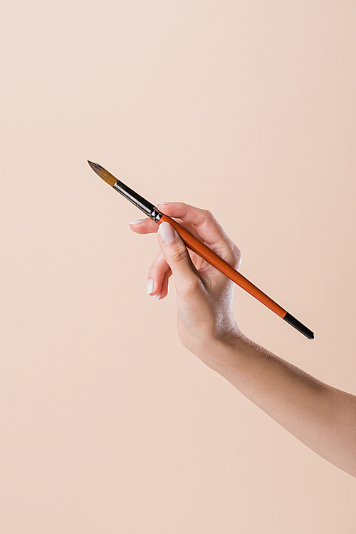 cropped shot of woman holding watercolor paint brush isolated on beige