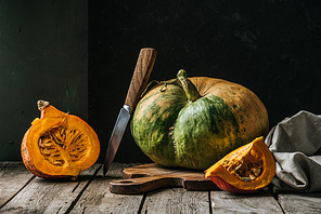 close up view of food composition with pumpkins, knife and cutting board on wooden surface on dark background
