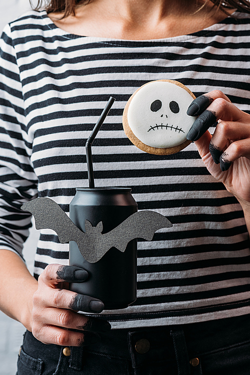 cropped shot of woman holding black can of soda and hallooween cookie