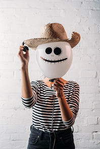 woman holding halloween balloon with straw hat in front of head