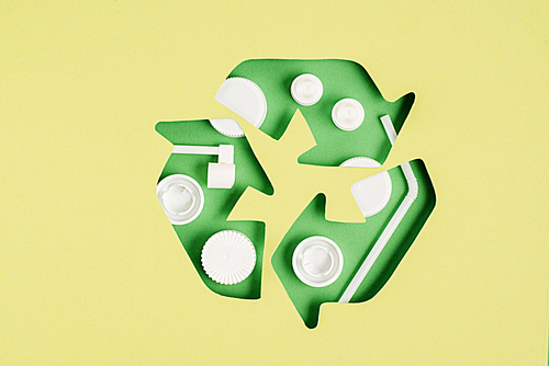 Top view of green recycle sign with bottle caps pattern on yellow background