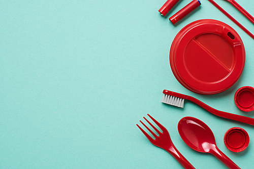 Top view of red plastic bottle caps, fork, spoon, lid for drink, batteries and toothbrush on blue background