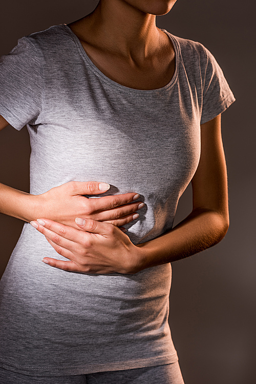 partial view of woman having liver ache on dark background