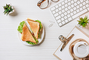 view from above of disposable coffee cup, sandwich, computer keyboard and eyeglasses at table in office