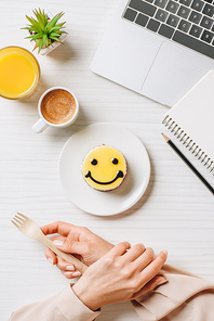 partial view of businesswoman eating cake with symbol of smile at table with orange juice and coffee cup in office