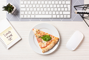 top view of pizza on plate, note with lunch time inscription, computer mouse and keyboard at workplace