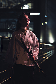 attractive asian girl in white kimono holding katana on street with neon light in evening, city of future concept
