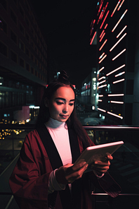 attractive asian girl in kimono using tablet on street with neon light in evening, city of future concept