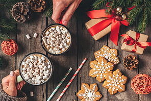 cropped view of couple holding cocoa cups with marshmallows and gingerbread on wooden background with christmas decor