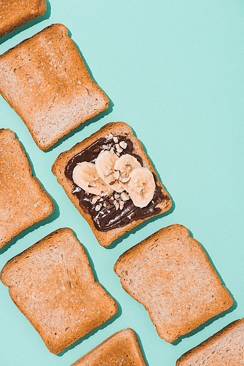 top view of toasts with chocolate paste and banana on blue surface