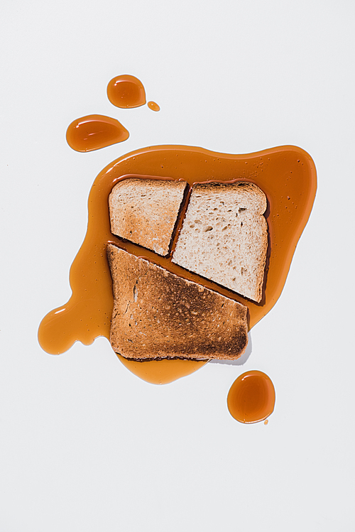 top view of slice of bread with roasted pieces on spilled brown syrup on white surface