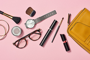 Top view of watch, bag, lipstick, glasses, eyeshadow, bracelets, mascara and cosmetic brushes on white background