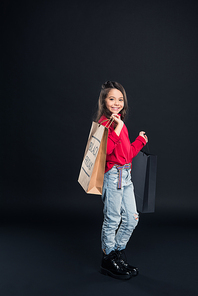 Smiling kid holding shopping bag on black friday and looking at the camera isolated on black