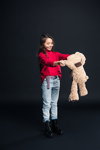 Smiling kid playing with teddy bear isolated on black