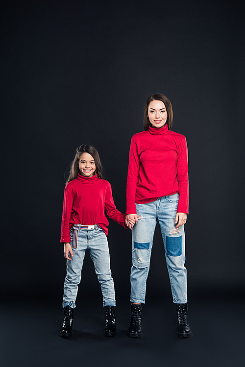 Mother and daughter standing and holding hands isolated on black