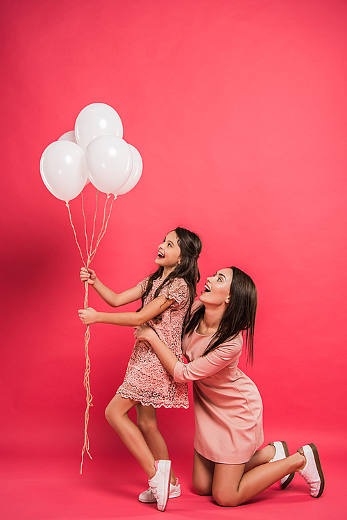 Daughter and mother looking at bundle of balloons on red