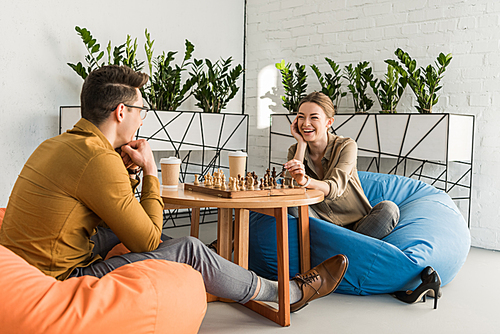 young happy friends playing chess while sitting on beanbags