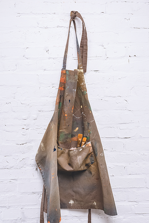 brown artist apron with paint brushes hanging on brick wall
