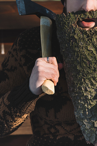 cropped shot of man with beard made of wood bark and axe in hand outdoors