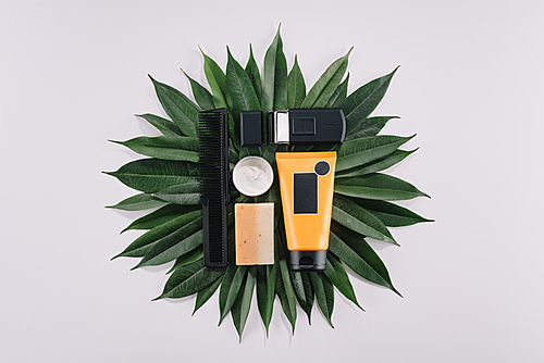 top view of arranged barber tools on green leaves isolated on grey