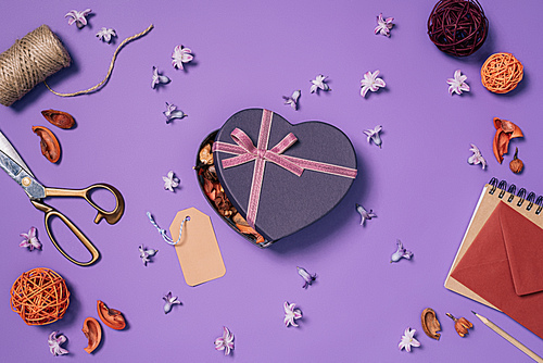 flat lay with heart shaped gift box, flowers, scissors, rope and envelope isolated on purple