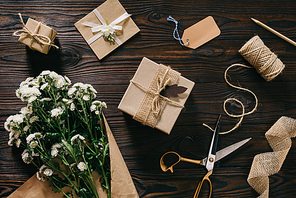 flat lay with wrapped presents, bouquet of flowers, rope and scissors on wooden surface