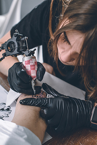 Female tattoo master in gloves with machine working on arm piece