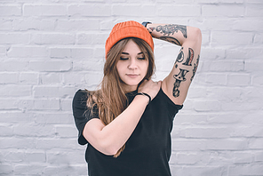 Young woman with tattooed arm standing next to white wall
