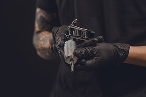 Male hands in gloves holding tattoo machine isolated on black
