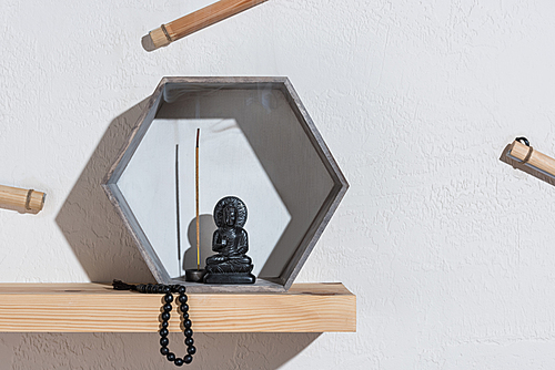 small statue of buddha in frame and rosary on wooden shelf