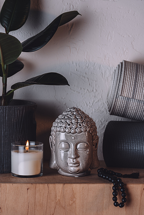 sculpture of buddha head, burning candle and yoga mats on wooden shelf