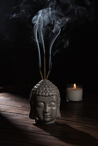 sculpture of buddha head with burning incense sticks and candle on table