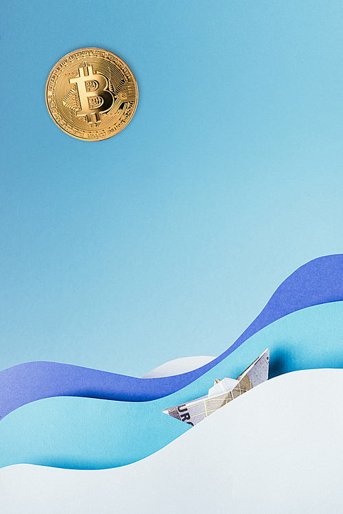close up view of golden bit coin and paper ship sailing on blue paper waves isolated on blue