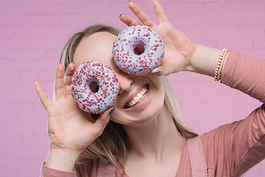 playful young woman covering eyes with doughnuts
