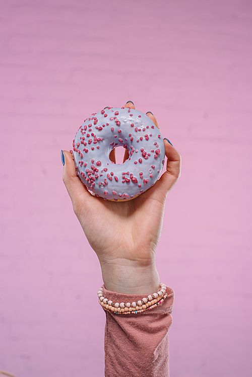 cropped shot of woman holding tasty glazed doughnut in hand