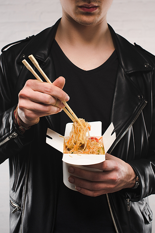 cropped shot of man in leather jacket holding chinese noodles in box